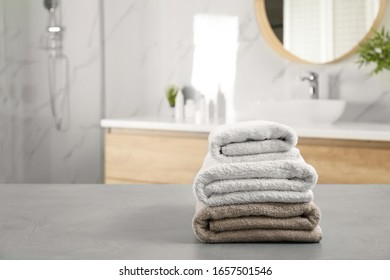 Stack of clean towels on grey stone table in bathroom. Space for text