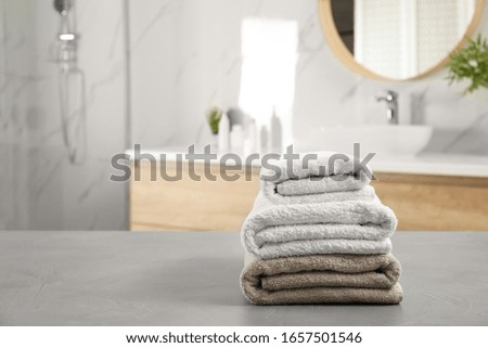 Stack of clean towels on grey stone table in bathroom. Space for text