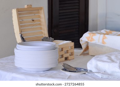 stack of clean white ceramic plates at buffet, dinnerware arrangement for catering event, pile of empty plates on restaurant table with wooden cutlery box, professional table setting for banquet service
