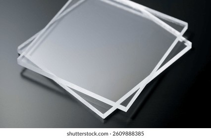 A stack of clear acrylic sheets placed on a dark surface, highlighting their transparency and smooth texture. Ideal for use in design, manufacturing, and construction projects.
