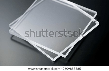 A stack of clear acrylic sheets placed on a dark surface, highlighting their transparency and smooth texture. Ideal for use in design, manufacturing, and construction projects.