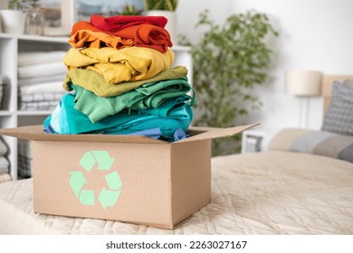 A stack of clothes in different colors in a box with a recycle sign. The concept of conscious clothing consumption.