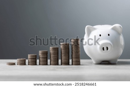 Stack of coins arranged from low to high alongside a white piggy bank on a wooden table against a gray background. The image symbolizes financial growth, savings, and building wealth step by step