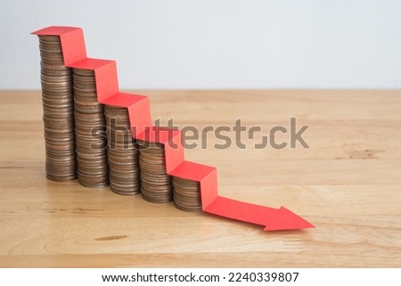 Stack of coins bar chart and red stair graph trending downwards with white wall background on wooden table copy space. Economy recession crisis, inflation, stagflation, business and financial loss.