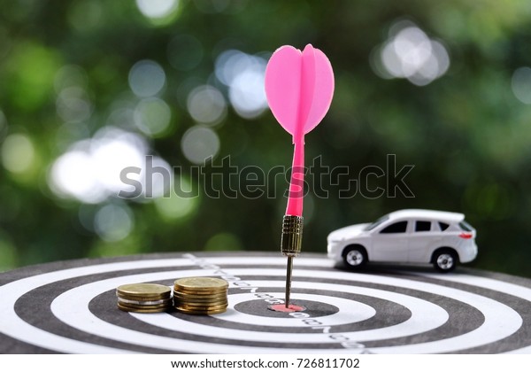 stack of\
coins and dart arrow hitting on target center of dartboard with toy\
car background, sucess and business\
concept