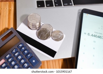 A stack of coins on credit cards next to the smartphone with a calculator app on the background of a notebook with the personal cabinet of the Internet Bank. Wooden office desk. Top view,flat lay