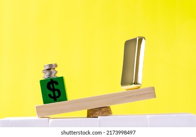 Stack Of Coins On The Cube With Dollar Sign Outweighing The Gold Bar On The Scales. Concept Of Unstable Currency Exchange Rates And Precious Metals Price