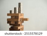 Stack coins on danger wood tower block game with white wall background copy space. Concept of business risk management, global economic crisis, financial bank run or bankruptcy, loss in investment.