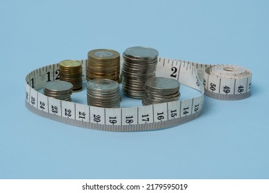 Stack Of Coins Surrounded By A Measuring Tape On The Blue Background. Price Increase, Economic Growth Concept.