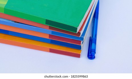 A stack of colored books and a pen lying on the table. A bunch of books