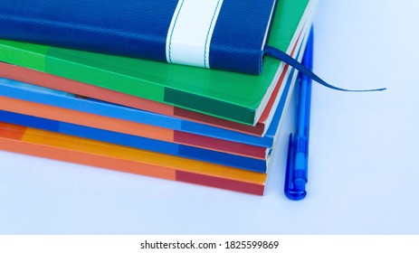 A stack of colored textbooks with notepad and a pen lying on the table. A bunch of books