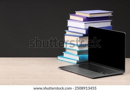 Stack of colorful books and laptop on white wooden table against black background, space for text