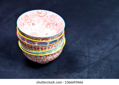 Stack of colorful empty ceramic bowls closeup on black board background. With copy space.