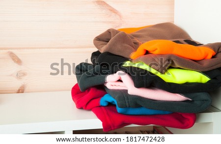 Stack of colorful fleece jackets laying on a white shelf in a wooden room interior