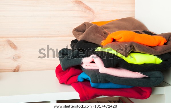 Stack of colorful fleece jackets laying on a\
white shelf in a wooden room\
interior