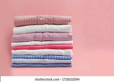 Stack of colorful perfectly folded clothing items. Pile of different pastel color shirts and sweaters isolated on pale pink background. Close up, copy space.