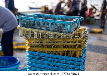 Stack of colorful plastic crates resting on busy bustling fish market dock reflecting hardworking energetic atmosphere near waterfront with workers handling fresh catch from boats in background