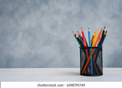 A stack of colorful textbooks and a glass of bright pencils on a gray- blue background. Concept of education , training, workspace, free space.