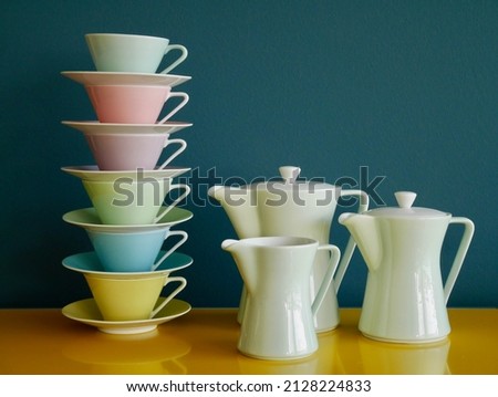 Stack of colorful vintage tea cups and tea pots on yellow table against petrol background. Afternoon tea party. High quality photo