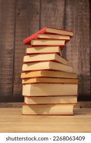 stack or column of red books forming a spiral and yellowish sheets of paper with dark wood background and light wood table vertical photo with space for text