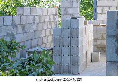 A stack of concrete cinder blocks is set up for construction in the backyard, with some greenery and trees visible around it