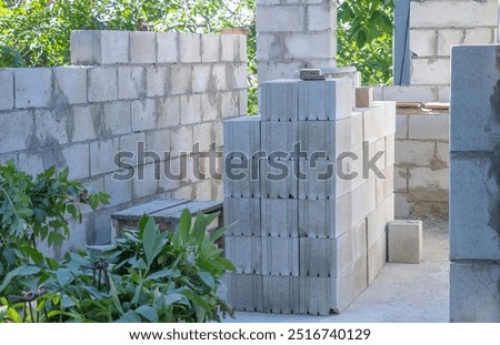 A stack of concrete cinder blocks is set up for construction in the backyard, with some greenery and trees visible around it