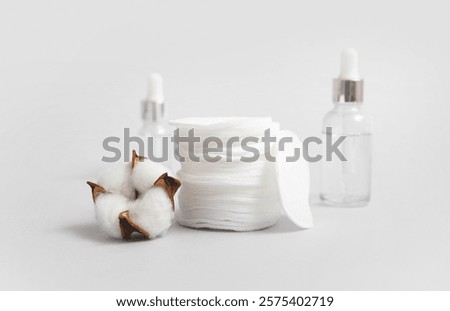 Stack of cosmetic pads, bottles of essential oil and cotton flower on color background