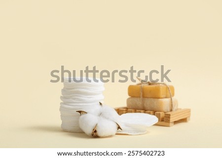 Stack of cosmetic pads, soap bars and cotton flower on color background