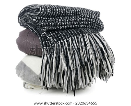 Stack of cozy home textiles: black and white knitted throw blanket with fringes, quilted brown blanket, and soft gray blanket