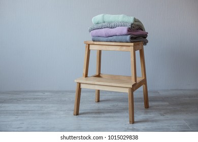Stack of cozy knitted clothes on a wooden ladder. Gray wall