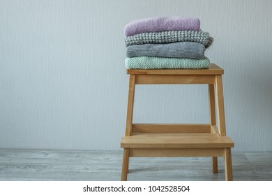 Stack of cozy knitted clothes on a wooden ladder. 