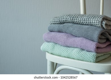 Stack of cozy knitted clothes on a wooden chair. Gray wall
