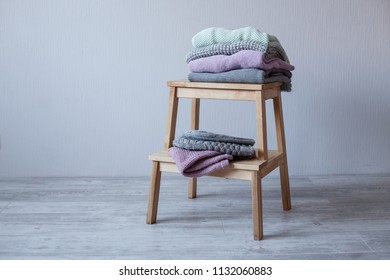 Stack of cozy knitted clothes on a wooden ladder. G