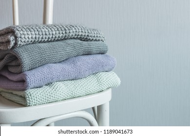 Stack of cozy knitted clothes on a wooden chair. Gray wall. Vintage tinting