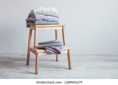 Stack of cozy knitted clothes on a wooden ladder. Gray wall. Vintage tinting