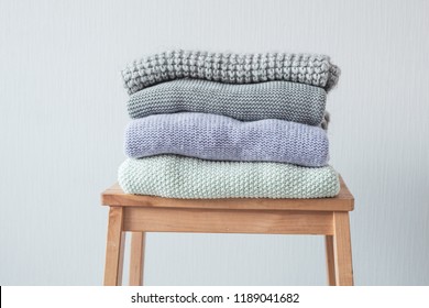 Stack of cozy knitted clothes on a wooden ladder. Gray wall. Vintage tinting