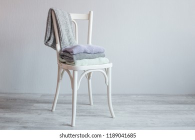 Stack of cozy knitted clothes on a wooden chair. Gray wall. Vintage tinting
