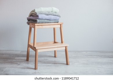 Stack of cozy knitted clothes on a wooden ladder. Gray wall. Vintage tinting