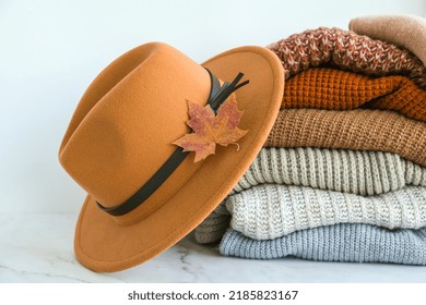 Stack Of Cozy Knitted Warm Sweater With Autumn Fall Maple Leaf And Beige Stylish Hat. Sweaters In Retro Style. Orange And Blue Colors. Cozy Hygge Concept Copy Space Autumn Season