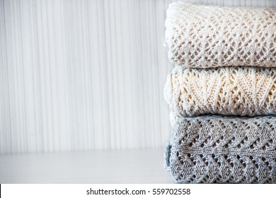 Stack of cozy knitted woolen clothes on the table. White, beige and grey sweater.