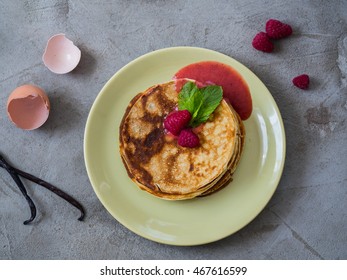 Stack Of Crepes (pancakes) With Raspberry Jam And Fresh Raspberries On Top, Eggshell, Vanilla Sticks And Fresh Raspberries On A Background, View From Above, Vertical. Protein Crepes. Beton Background