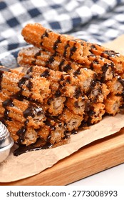 Stack of crispy churros covered in chocolate syrup on a wooden table