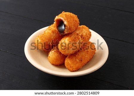 Stack of crispy fried glutinous rice cakes with oozing black brown sugar filling in a bowl, dark wooden background
