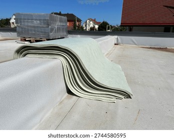 A stack of cut protective material sheets folded on the parapet of a flat membrane roof. These pads are used to be placed under concrete ballast blocks to prevent damage to the roof's waterproofing layer during solar panel installation
