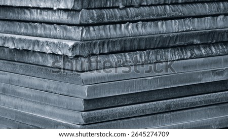 Stack of dark blue thick heavy metal plates rusty uneven surface after laser cutting. plates stacked top each other, creating sense depth and texture. scene is somewhat dark industrial blue background