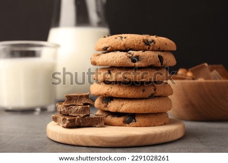 Stack of delicious chocolate chip cookies and milk on grey table