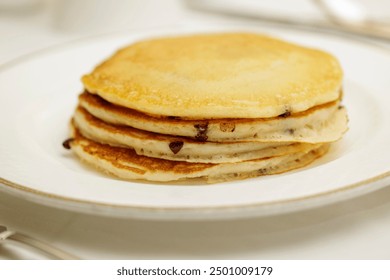 A stack of delicious golden-brown pancakes with chocolate chips on a white plate. - Powered by Shutterstock