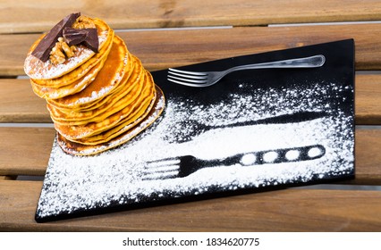 Stack of delicious pancakes with chocolate and walnuts on black plate..