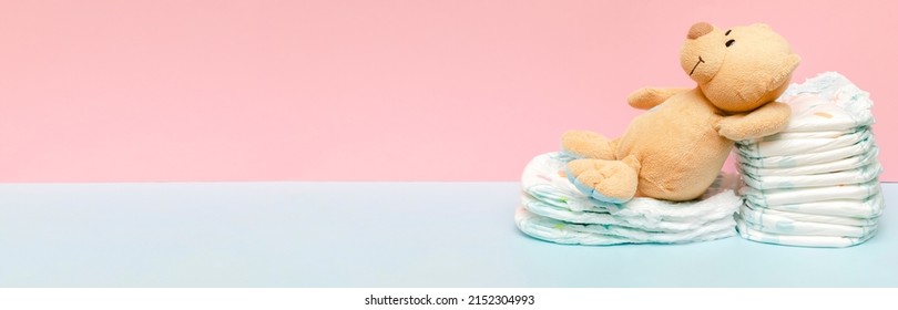 Stack of diapers with cute teddy bear toy lying on table. set for infant newborn boy girl for baby shower present gift on blue pink background with copy space. Healthcare medical, hygiene concept.