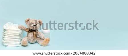 Stack of diapers with cute teddy bear toy, bottle of milk on table. set for infant boy girl for baby shower present gift on blue background, banner, copy space. Healthcare medical, hygiene concept.